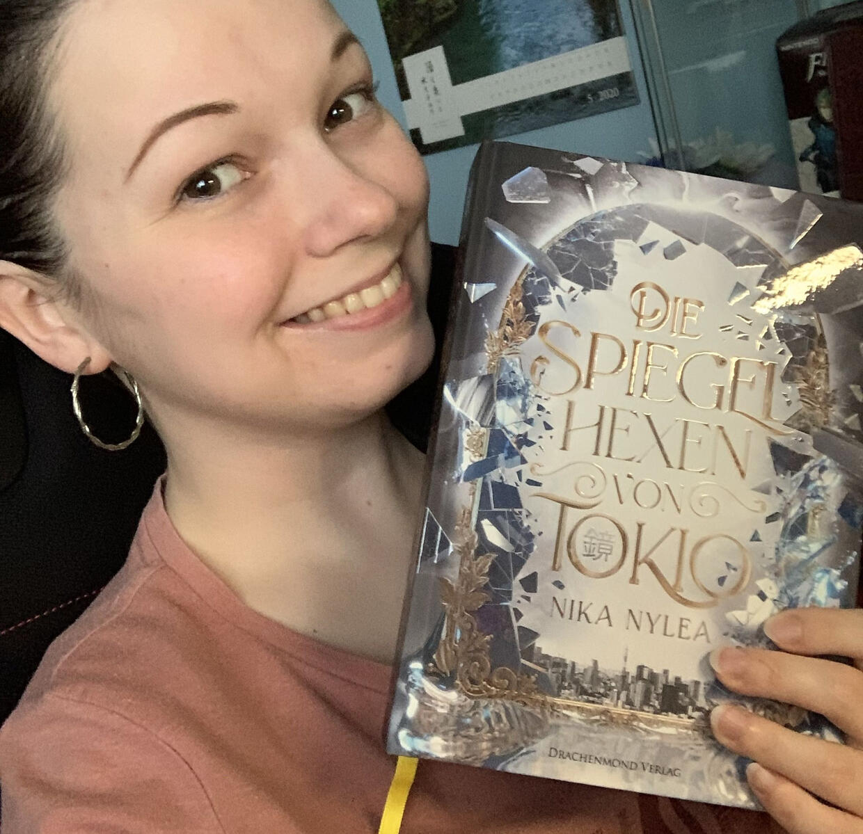 Nika und die Spiegelhexen Nika in ihrem Zimmer mit einem Hardcover von "Die Spiegelhexen von Tokio" in der Hand.